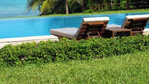 A poolside area with lounge chairs, a palm tree, and a thatched-roof structure. - Zawadi Hotel Zanzibar - All Inclusive (Dongwe)