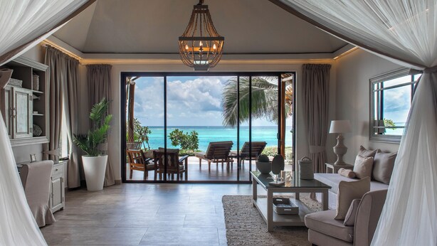 A spacious living area with a large sliding glass door leading to a balcony overlooking the ocean. - Zawadi Hotel Zanzibar - All Inclusive (Dongwe)