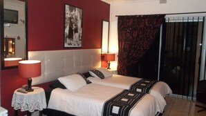 Ein Hotelzimmer mit zwei Betten, einer roten Wand, einem gerahmten Bild, einem Spiegel und einem Vorhangfenster.