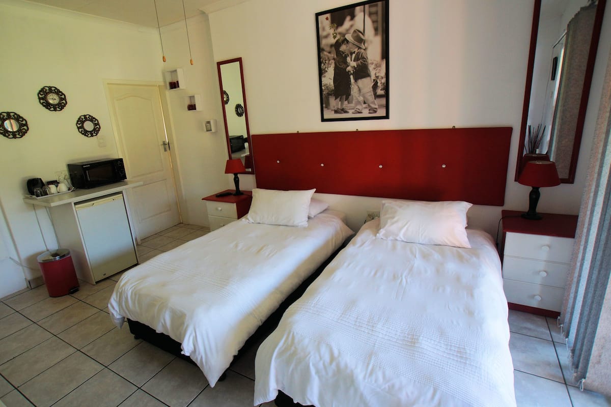 Ein Hotelzimmer mit zwei Betten, einem Schreibtisch mit Mikrowelle, einem roten Kopfteil, einem Spiegel und einem gerahmten Bild an der Wand.