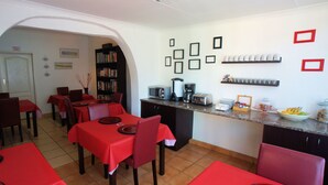 Ein Essbereich mit roten Tischen und Stühlen, eine Küche mit Geräten und ein Bücherregal.