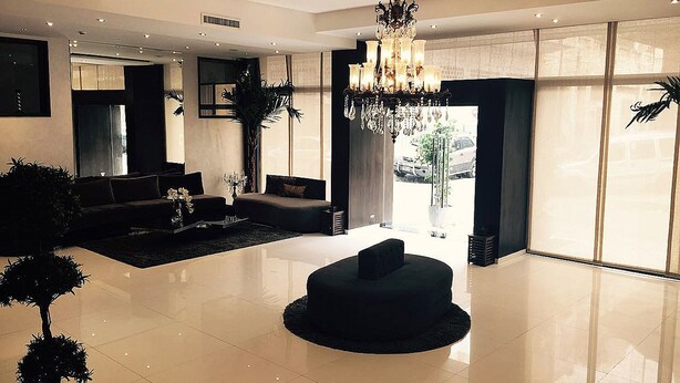 A spacious living area with a modern chandelier, a black sofa, and a round black ottoman. - The Seven Hotel and Spa (Casablanca)