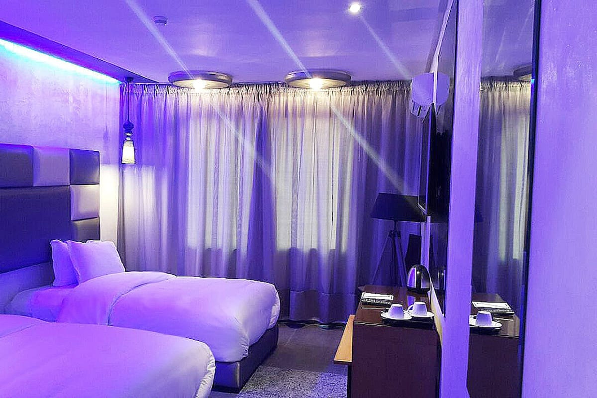 A hotel room with two beds, a nightstand, a lamp, and a mirror.