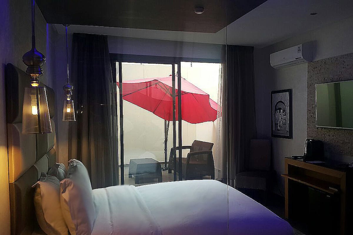 A hotel room with a bed, a desk, a chair, a red umbrella, and a window.