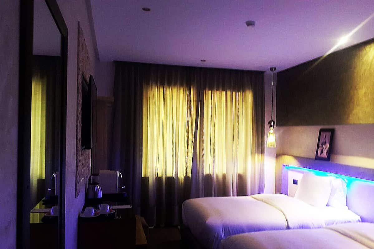A hotel room with a bed, a desk with a lamp, and a window with curtains.