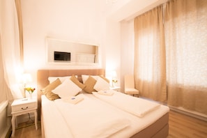 A hotel room with a large bed, two bedside tables, a TV mounted above the bed, and a window with curtains.