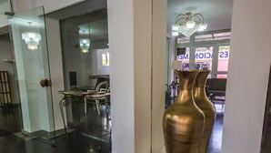 Un vestíbulo moderno con un separador de vidrio, una araña y dos grandes jarrones sobre pedestales.