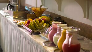 Una mesa de buffet con frutas, bebidas y una cafetera.