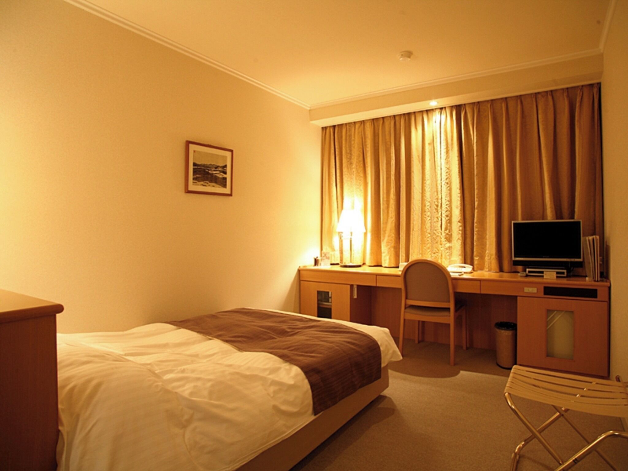 Habitació d'hotel amb llit, escriptori, cadira, televisió i làmpada.