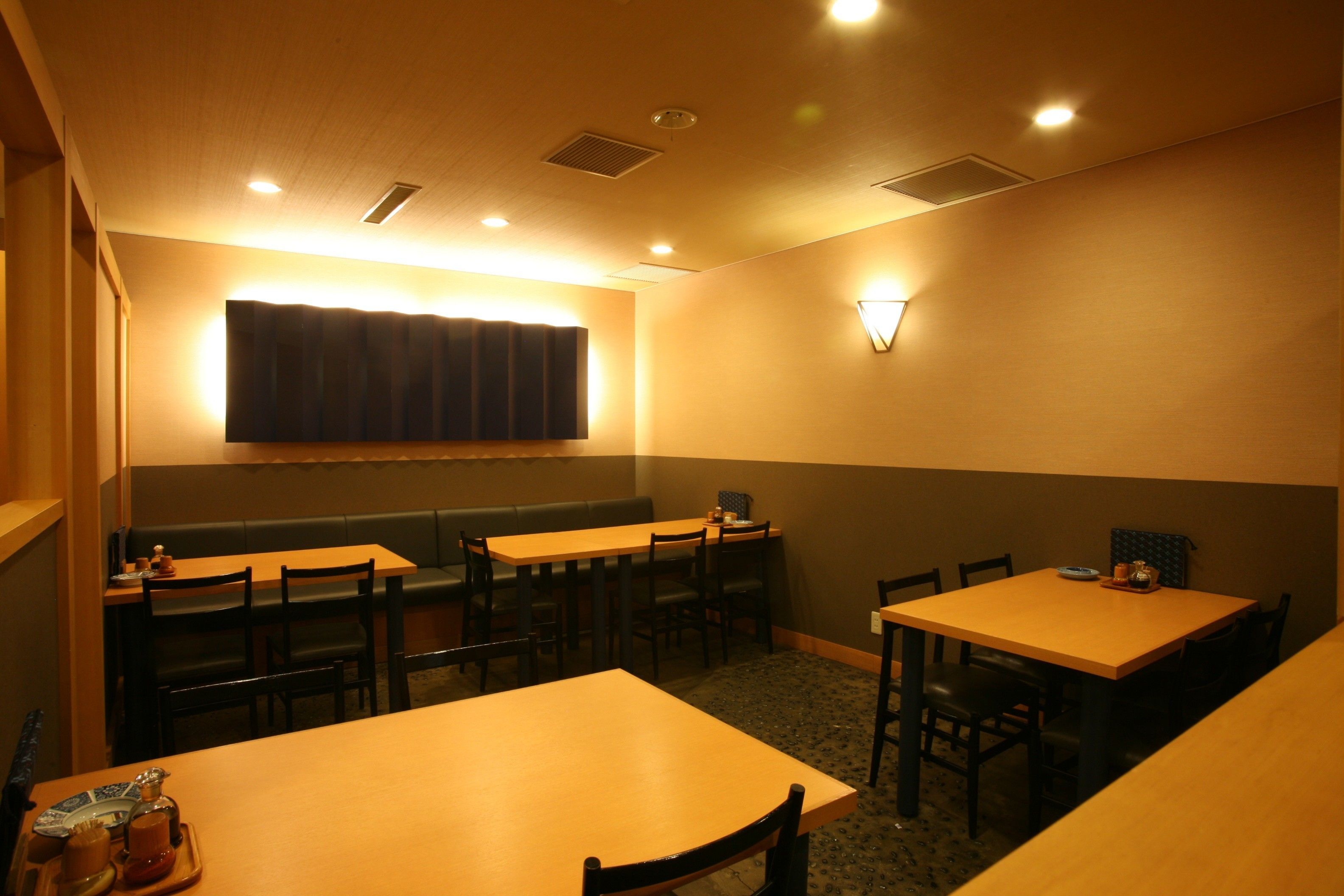 A dining area with multiple tables and chairs, a large window with curtains, and a wall-mounted light fixture.