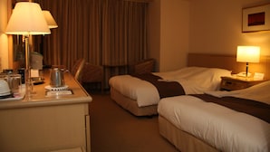 A hotel room with two beds, a desk with a lamp, a coffee maker, and a chair.
