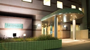 A hotel entrance with a covered waiting area, a sign with Japanese characters, and a tiled planter in the foreground.