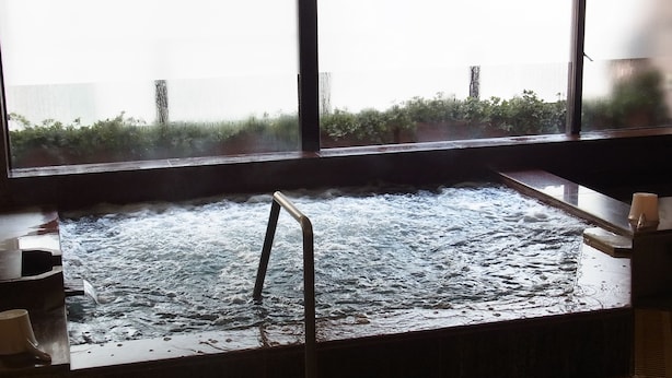 A hot tub with a metal ladder, a wooden bench, and a window with a view of greenery outside.