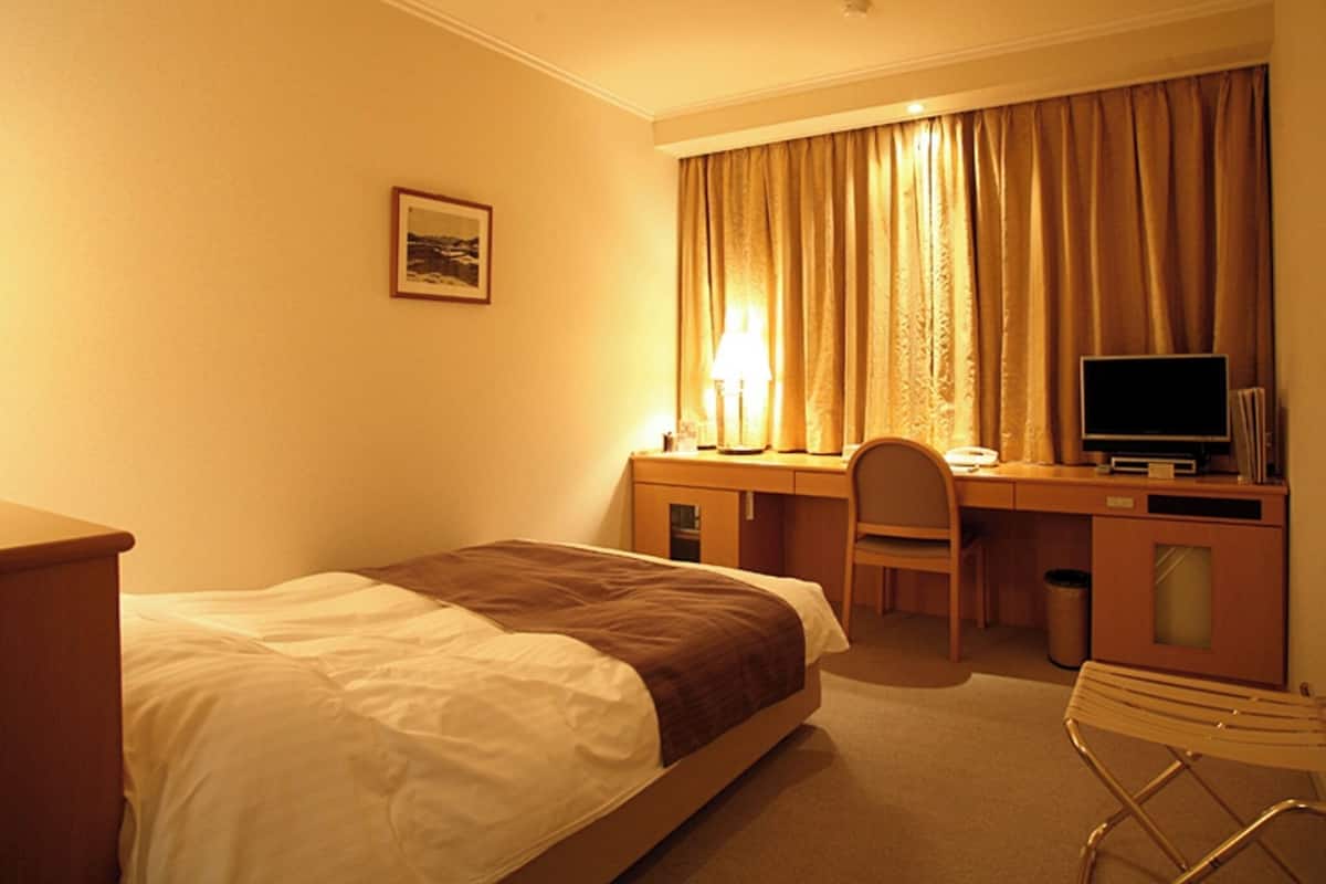 Una habitación de hotel con cama, escritorio, silla, televisor y lámpara.