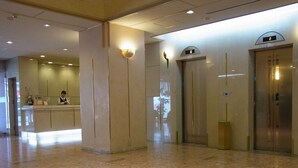 A lobby with a reception desk, two elevators, and a tiled floor.