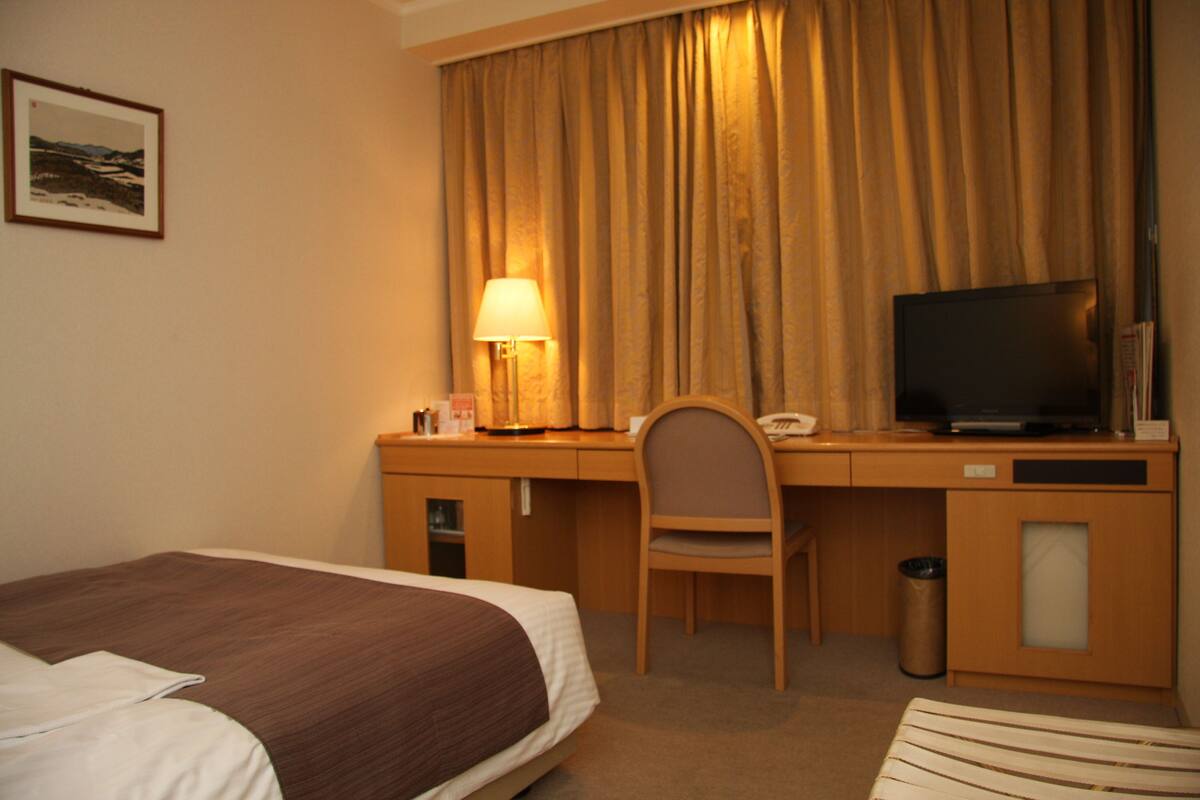 Una habitación de hotel con una cama, un escritorio con televisor, una silla y una lámpara.