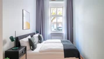 A neatly arranged bedroom with a bed, bedside table, lamp, and a window with curtains.