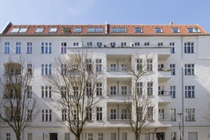 Un edificio residencial de varios pisos con techo de tejas rojas, varios balcones y una hilera de ventanas.