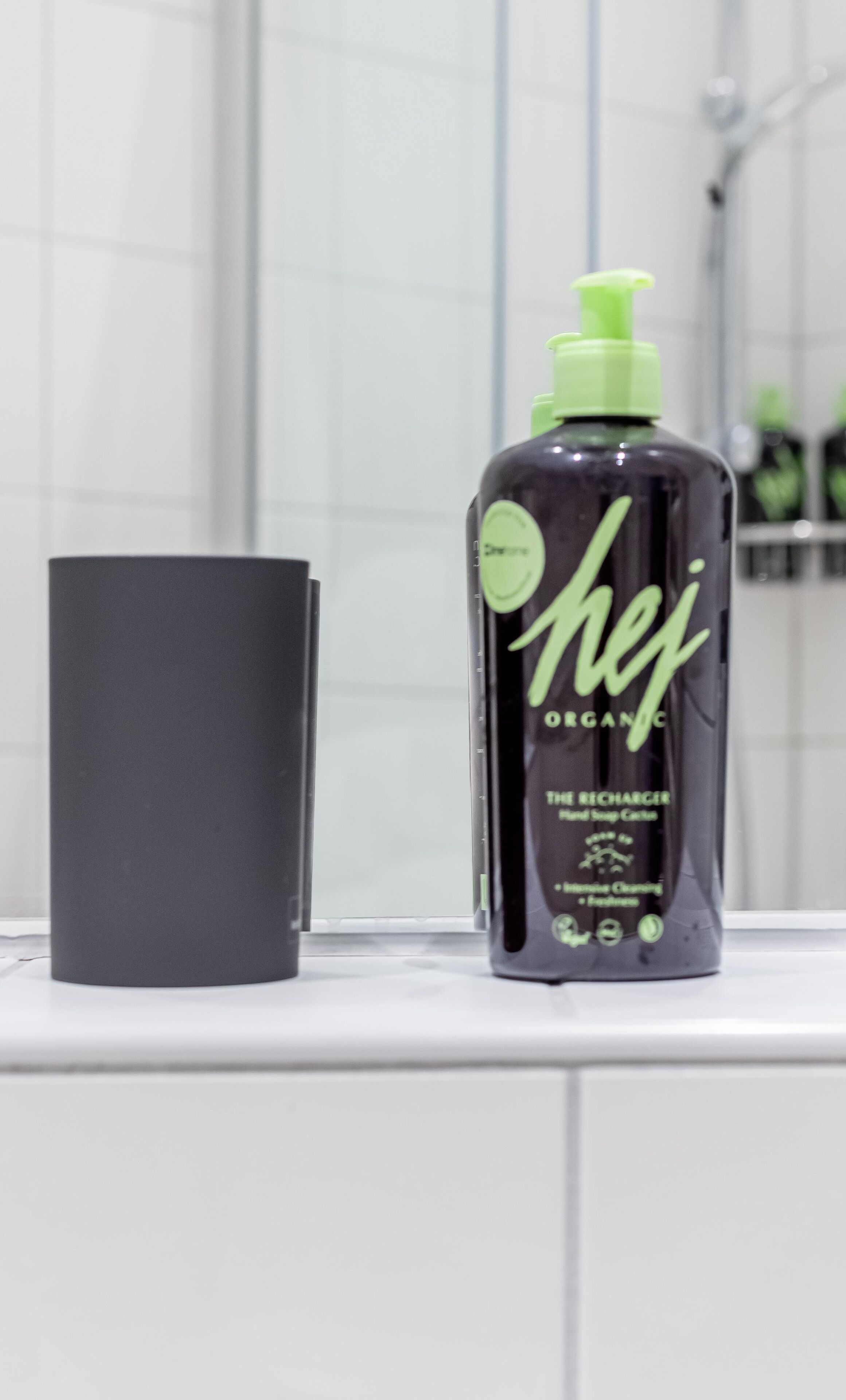 A bathroom with a black bottle of organic hand soap and a black container on a white countertop.