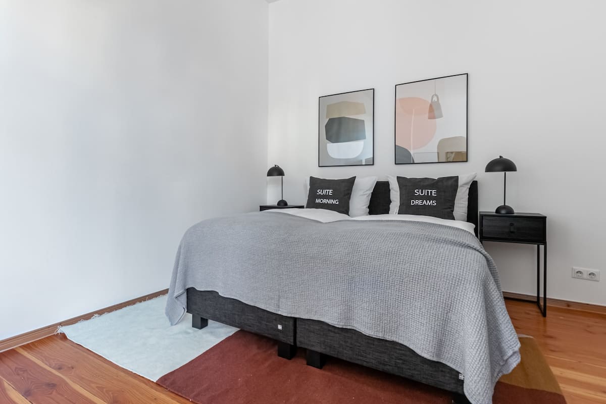 A bedroom with a bed, bedside tables, and two wall-mounted lamps.