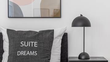 Un dormitorio ordenado con cama, una mesita de noche con lámpara y una obra de arte abstracta enmarcada en la pared.