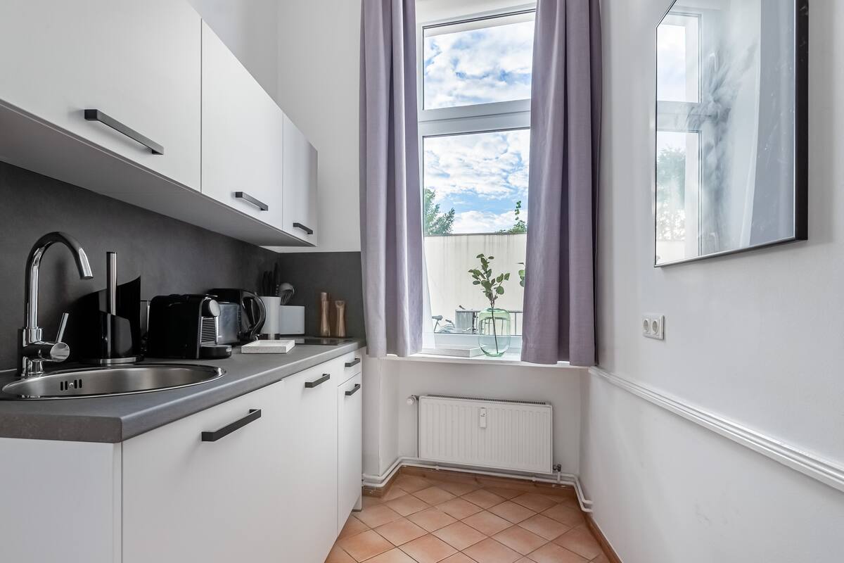 A modern kitchen with white cabinets, a stainless steel sink, and a window with purple curtains.