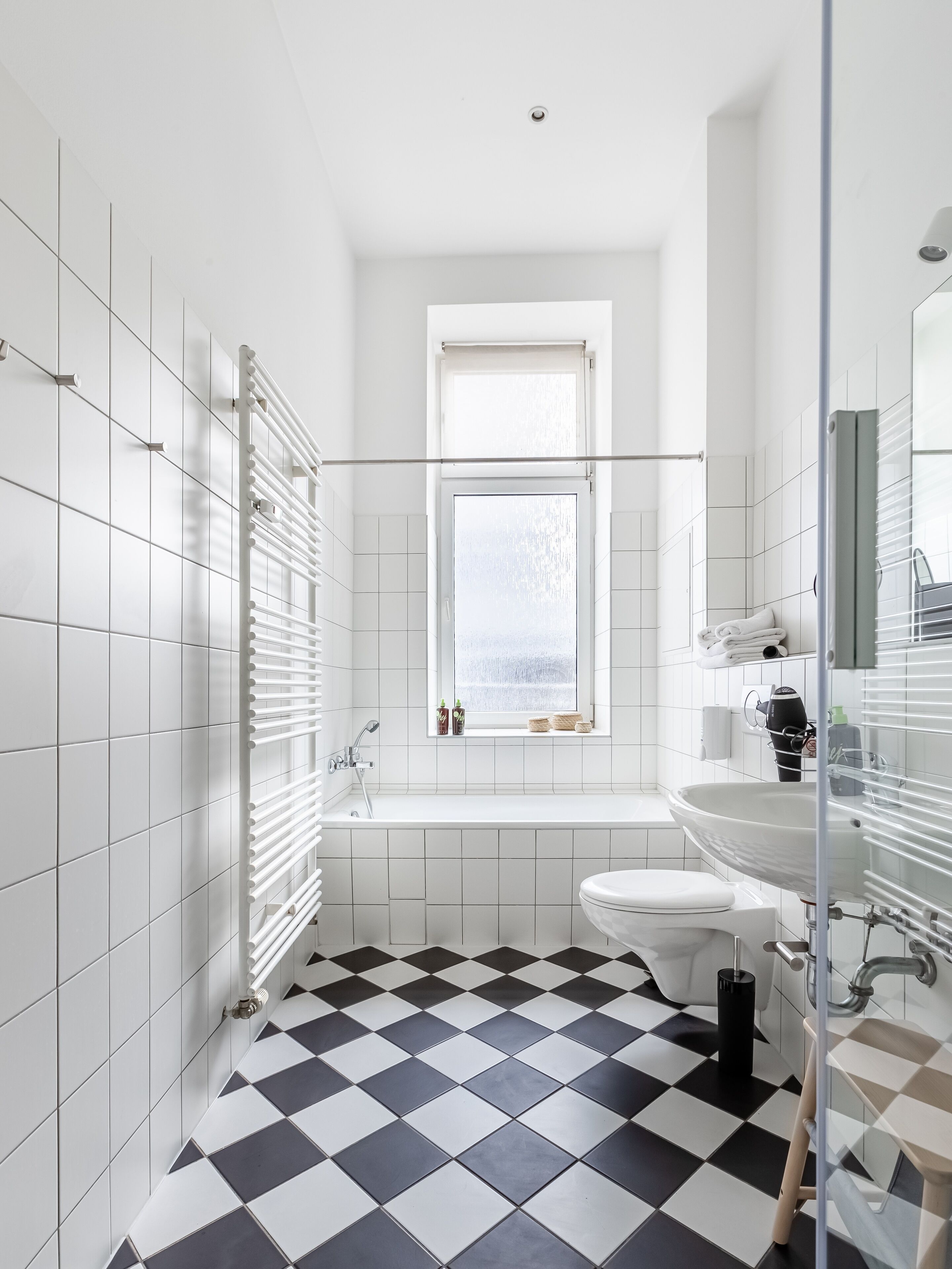 Une salle de bain moderne avec un carrelage noir et blanc à motifs, une baignoire blanche, des toilettes blanches et une cabine de douche en verre.