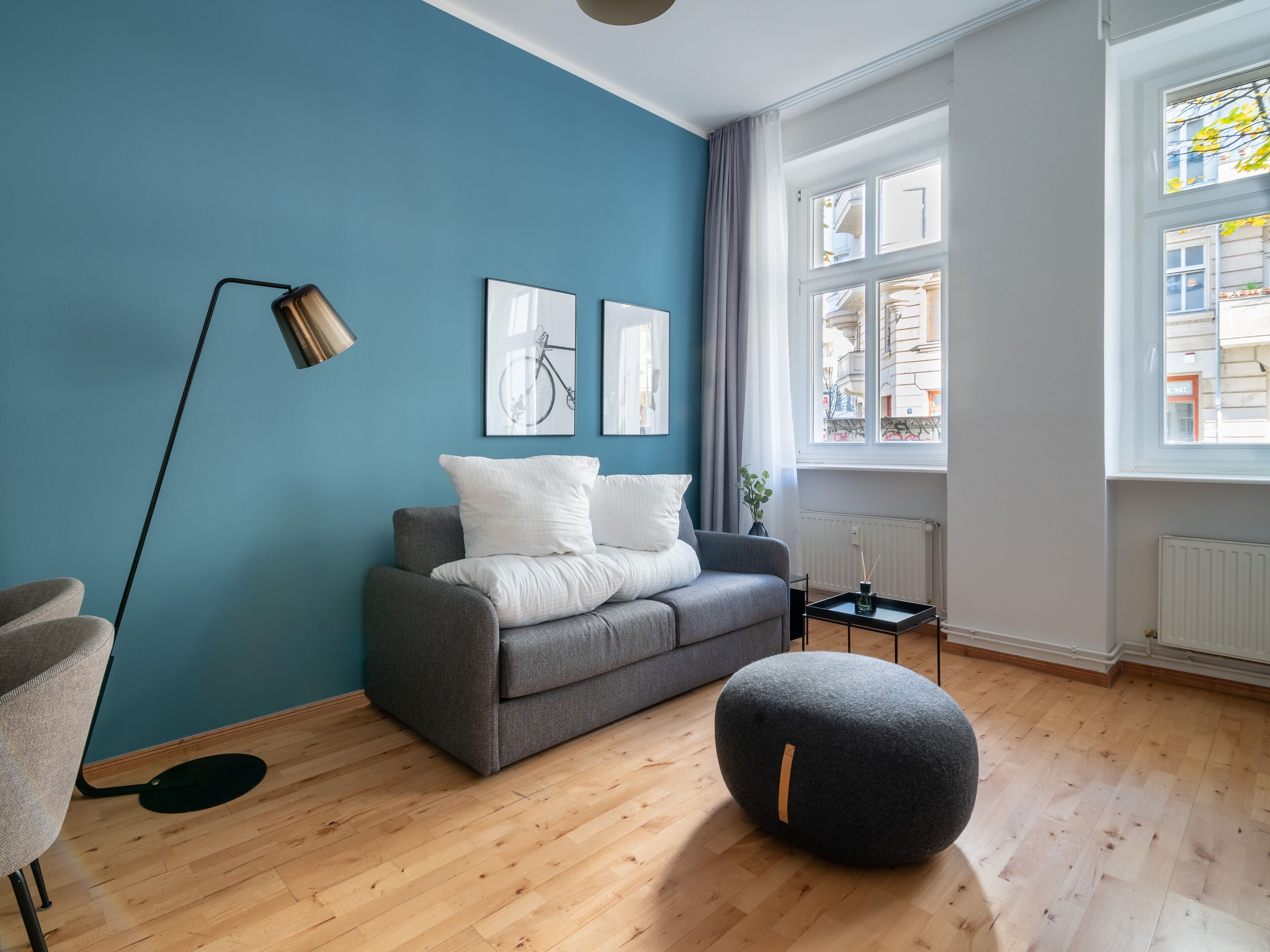 Una sala de estar moderna con un sofá gris, un otoman redondo y una lámpara de pie.