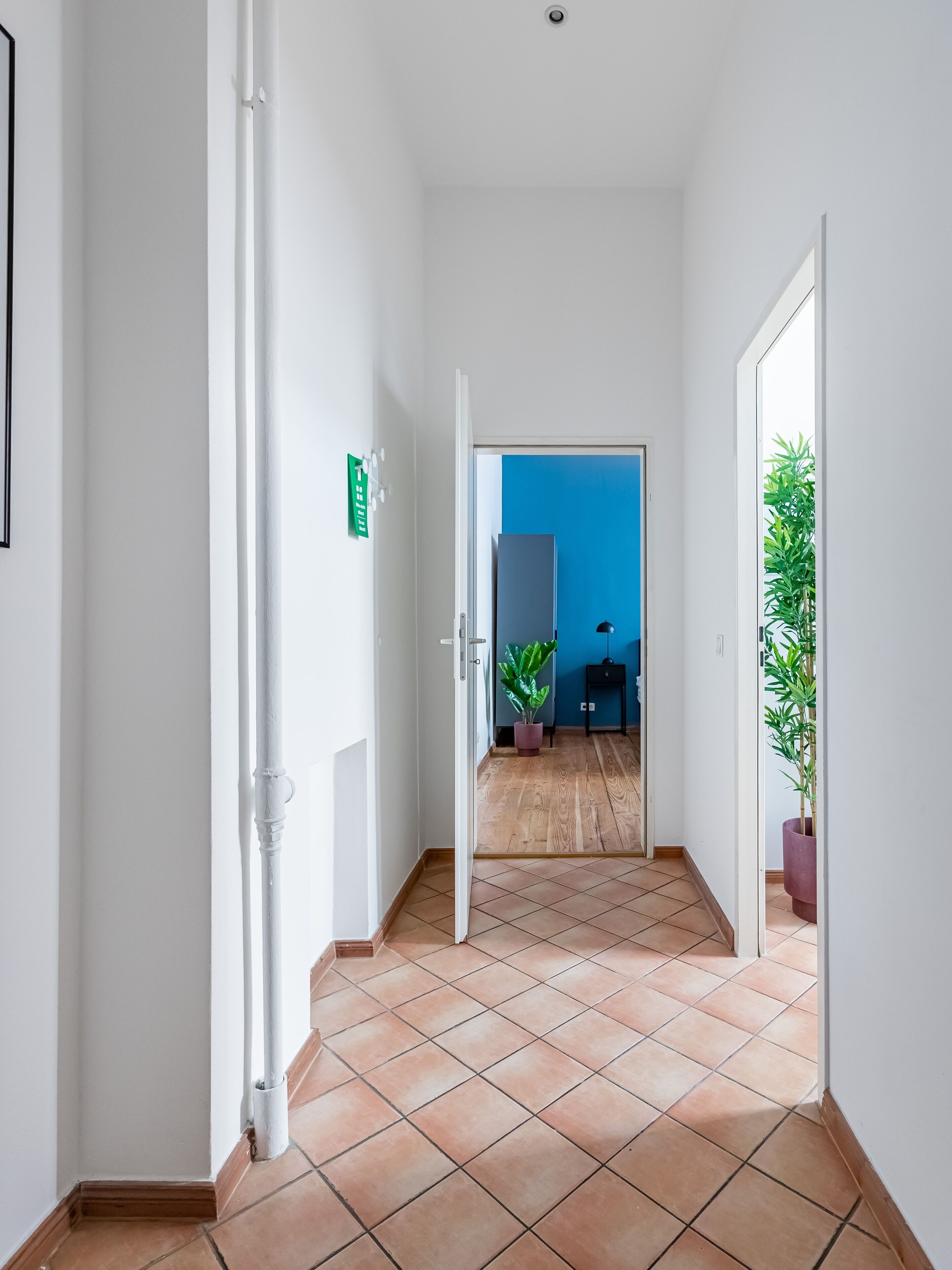 A hallway with a tiled floor, white walls, and a blue door at the end.