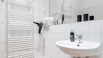 A modern bathroom with a white tiled floor, a white sink with a chrome faucet, and a towel rack with folded towels.