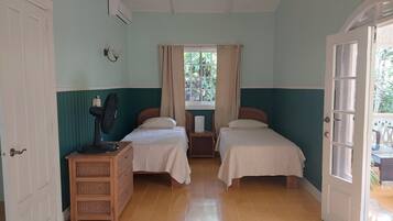 Una habitación con dos camas, un ventilador, una mesita y una ventana con cortinas.