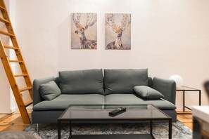A living room with a grey sofa, a glass coffee table, and two wall-mounted paintings of deer. - Apartments am Görlitzer Park (Berlin)