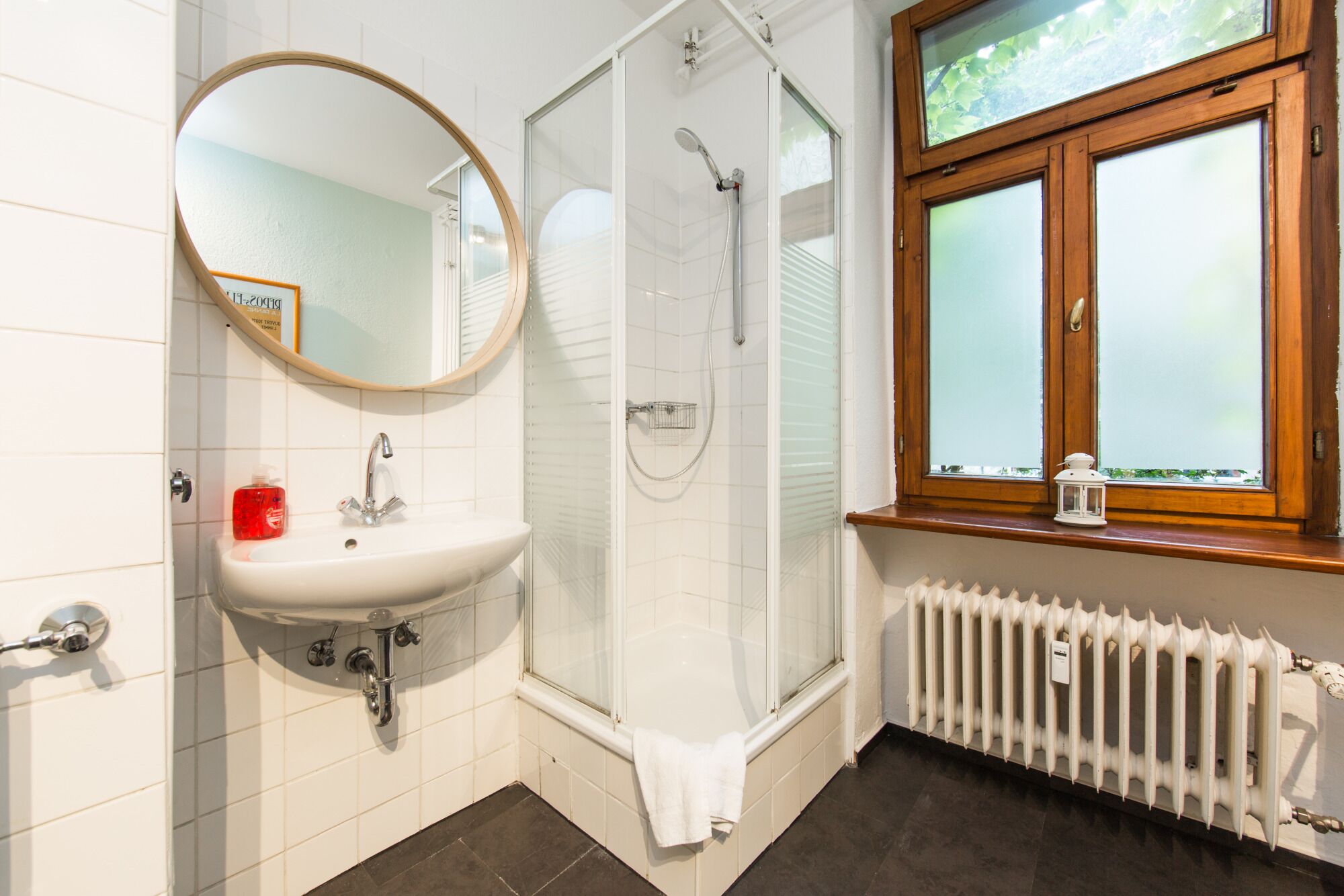A bathroom with a white sink, a mirror, a shower, and a window with frosted glass.
