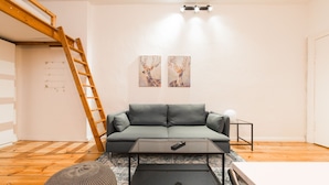 Ein Wohnzimmer mit grauem Sofa, einem Couchtisch, einer Leiter und zwei an der Wand hängenden Bildern.