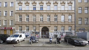 Ein Gebäude mit mehreren Fenstern und einer Tür, umgeben von parkenden Autos und Graffiti.