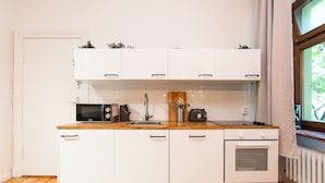 Eine kompakte Küche mit weißen Schränken, einer Mikrowelle, einem Wasserkocher und einem Toaster.