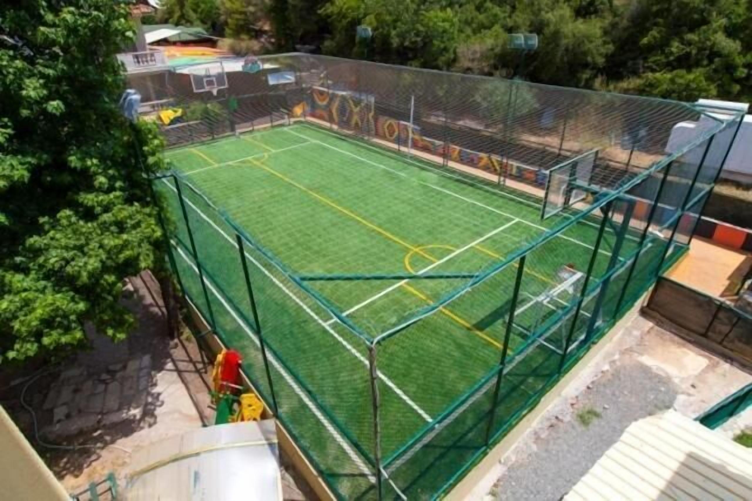 A fenced outdoor sports court with a green surface, surrounded by a metal fence.