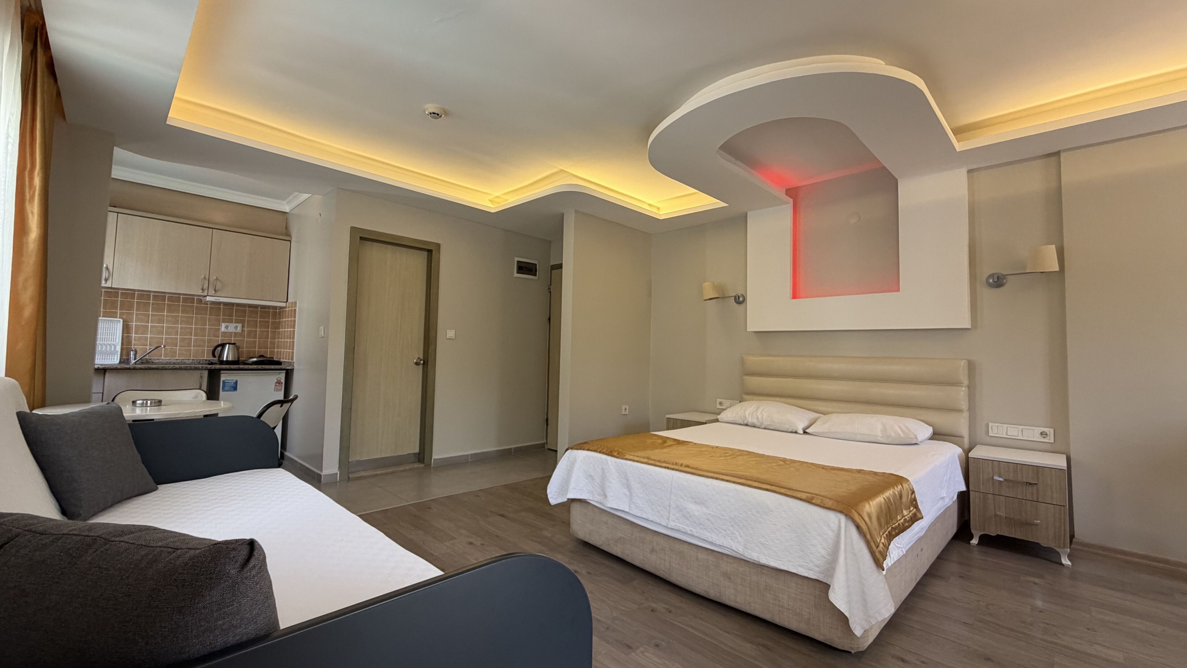 A hotel room with a bed, a sofa, a small kitchenette, and a bathroom.