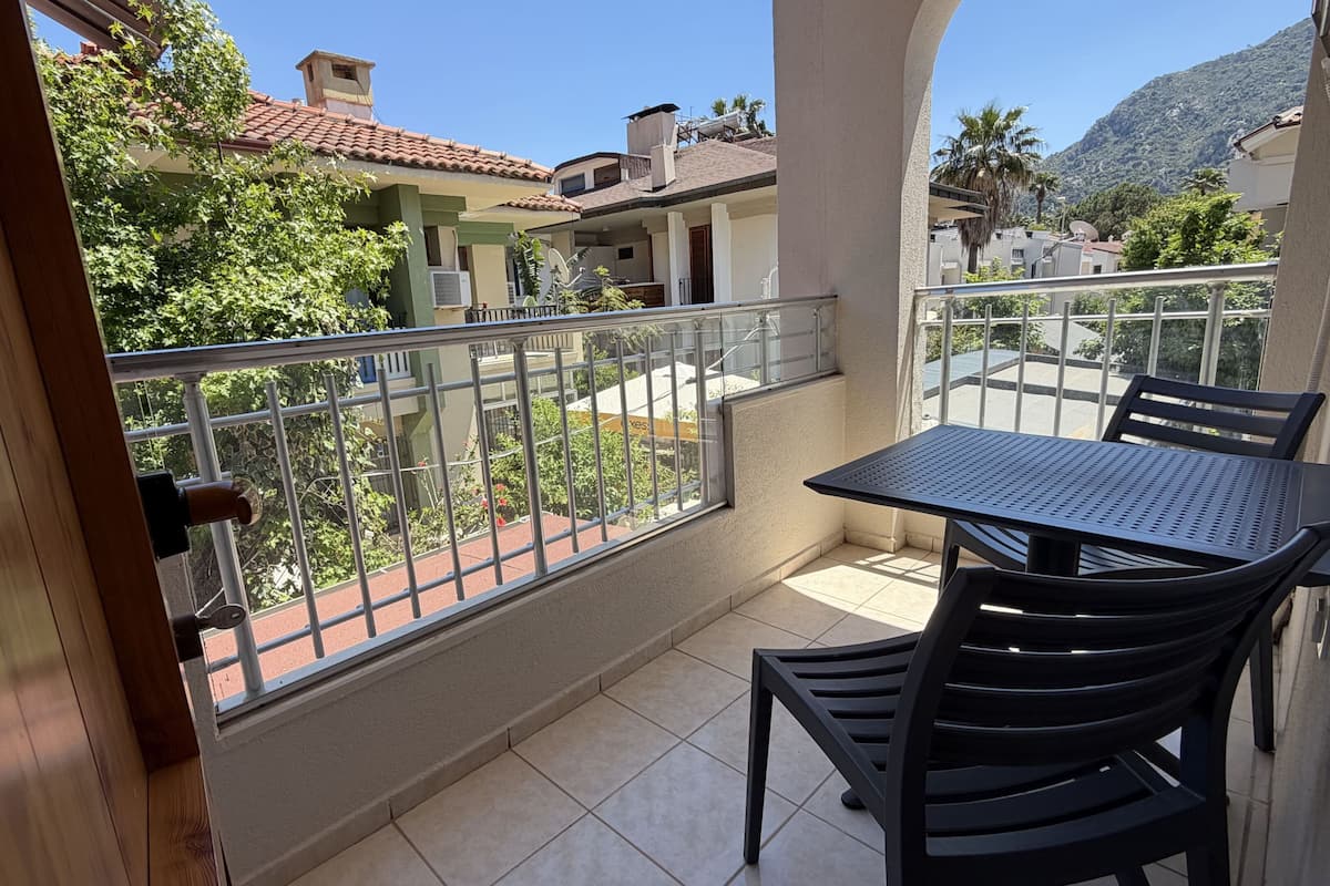A balcony with a table and chairs, a metal railing, and a view of neighboring buildings and greenery.