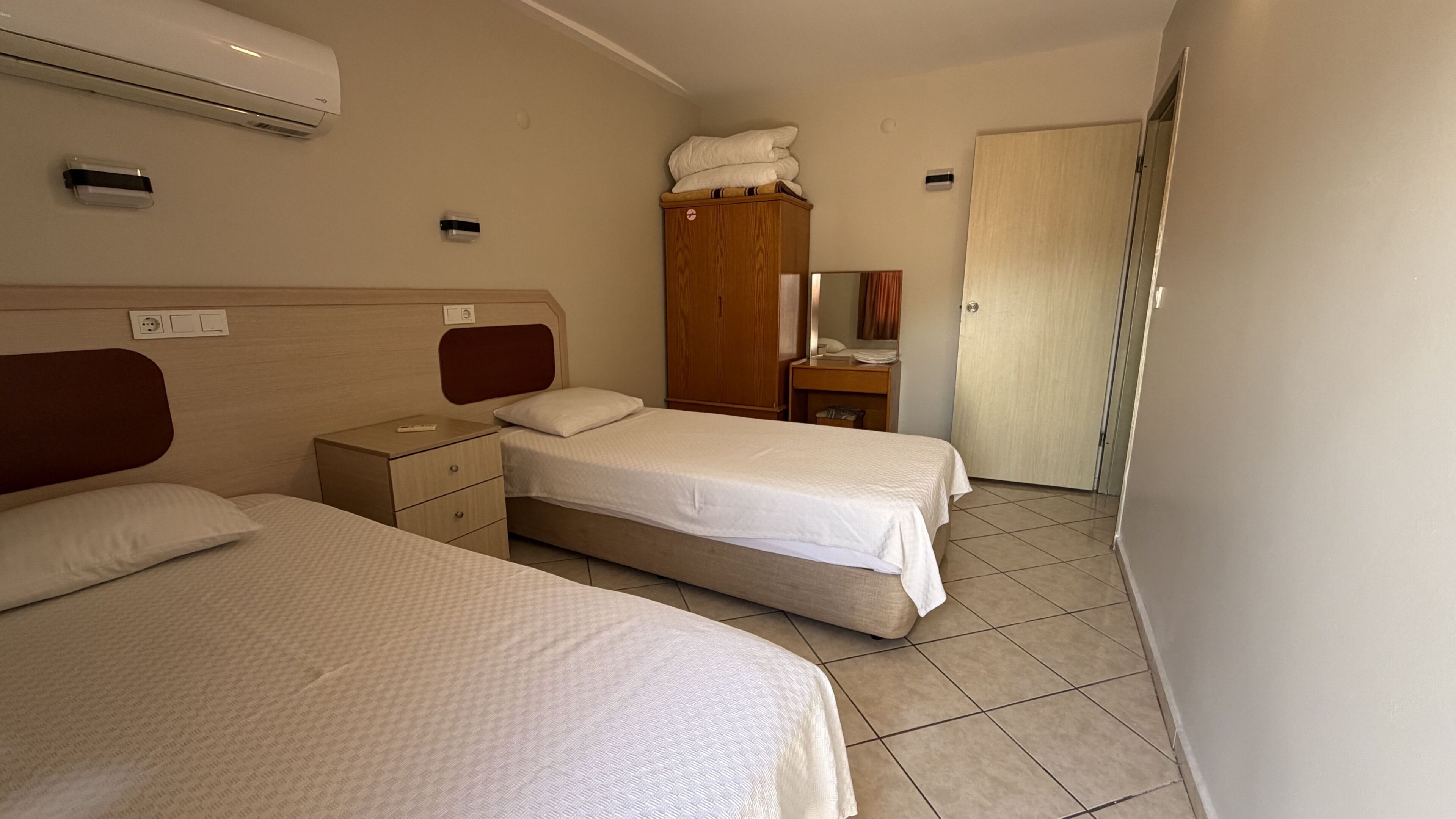 A hotel room with two beds, a wardrobe, a bedside table, and a bathroom door.