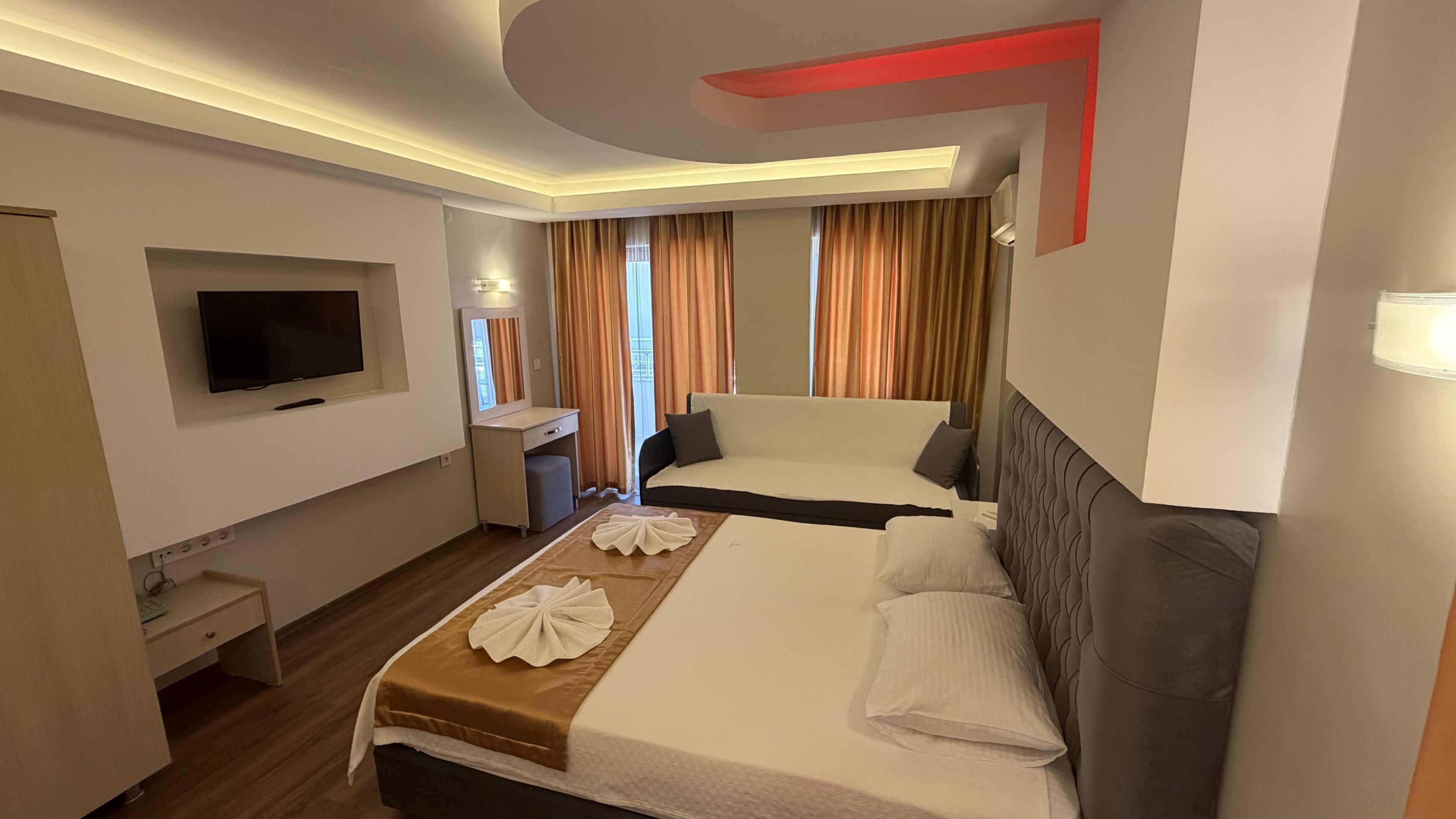 A hotel room with a bed, a desk, a TV, and a window with curtains.