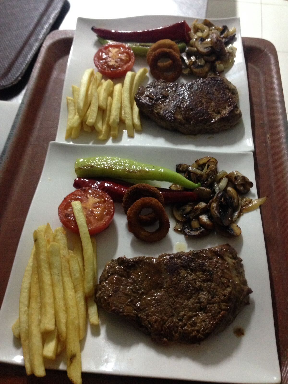 A tray with two plates of food, each containing a steak, fries, and various vegetables.