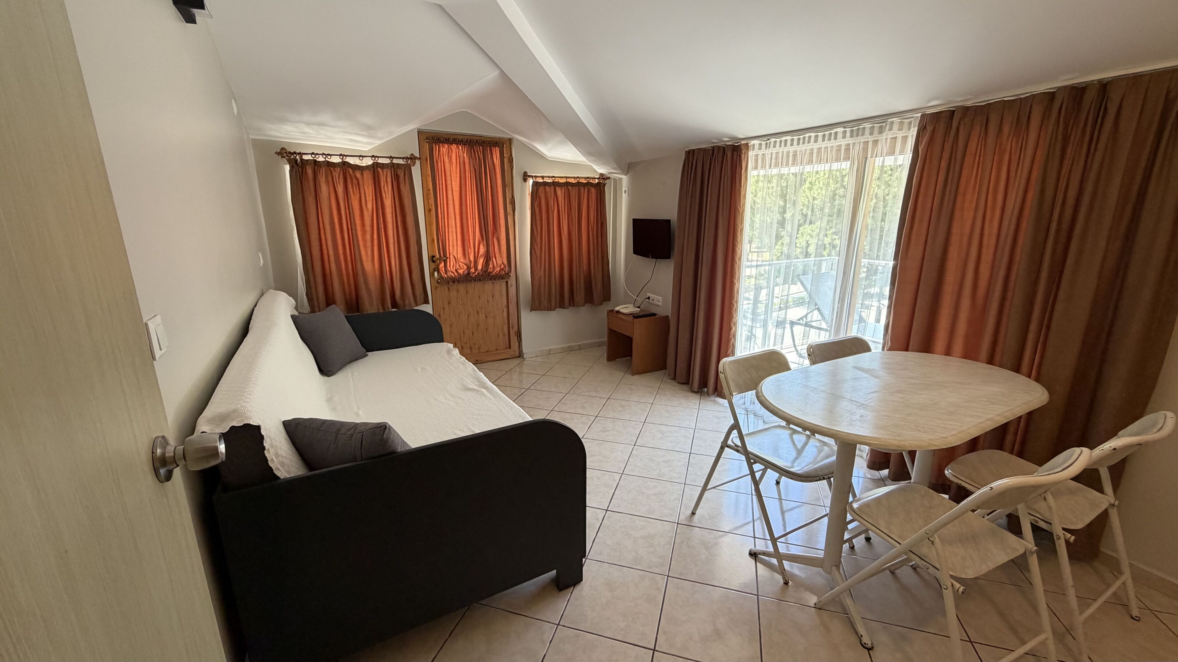 Una habitación con cama, escritorio, silla, mesa y ventana con cortinas.