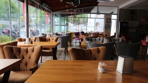 A restaurant interior with wooden tables and chairs, large windows, and a view of the street outside. - Arya Apart (Marmaris)