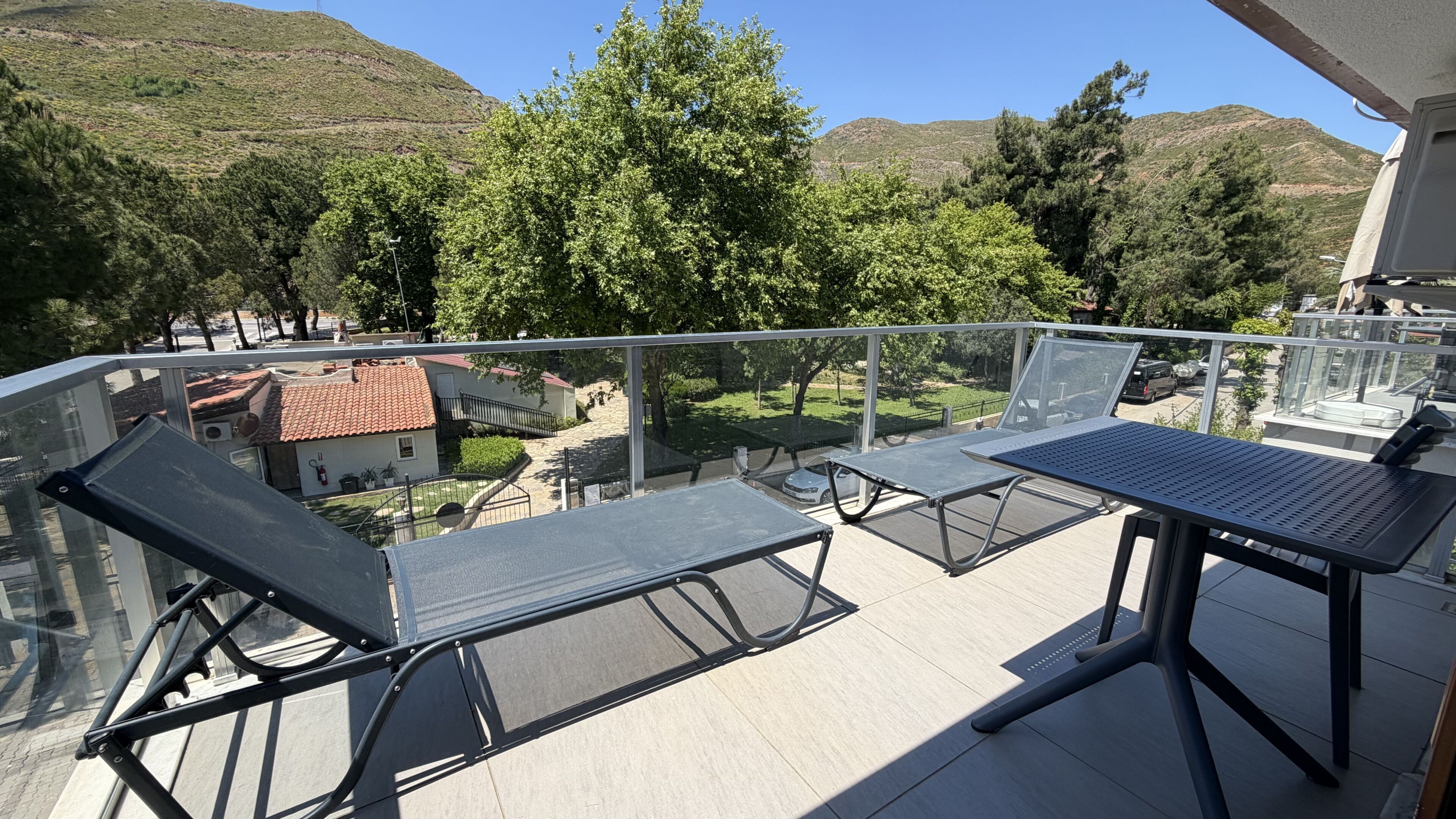 Ein Balkon mit Tisch und Stühlen, mit Blick auf ein Wohngebiet mit Häusern und Bäumen.