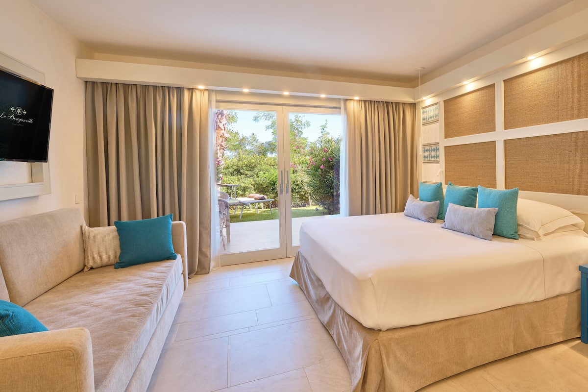 Een hotelkamer met een groot bed, een bank, een televisie en een balkon met gordijnen.