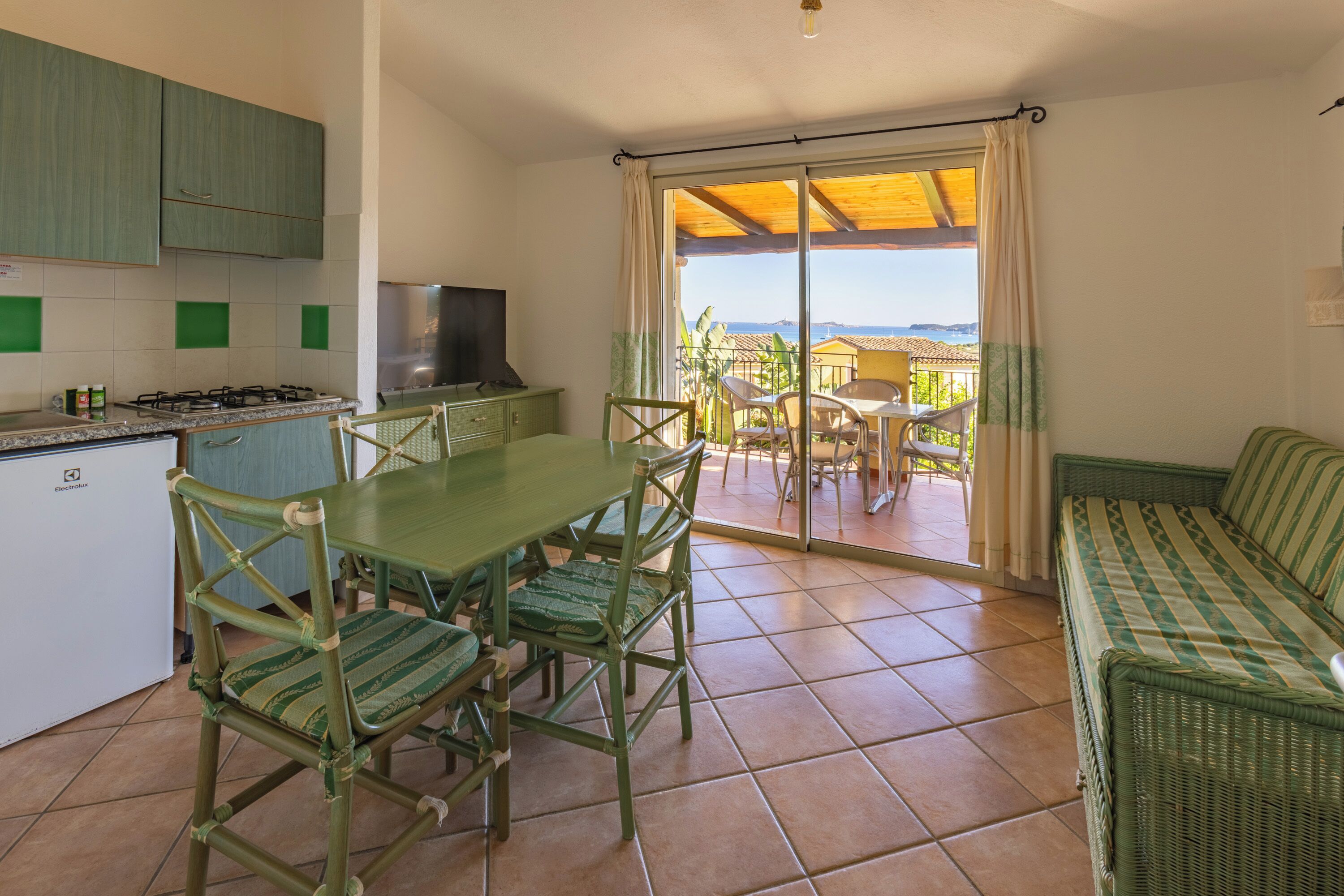 Une cuisine avec une table et des chaises, un canapé et une porte-fenêtre coulissante donnant sur une terrasse extérieure.