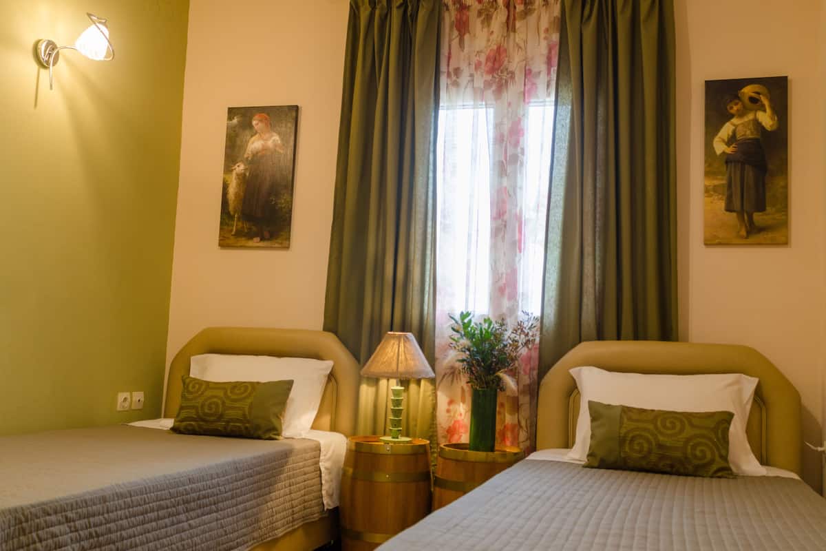 A room with two beds, a lamp, a vase with flowers, and two paintings on the wall.