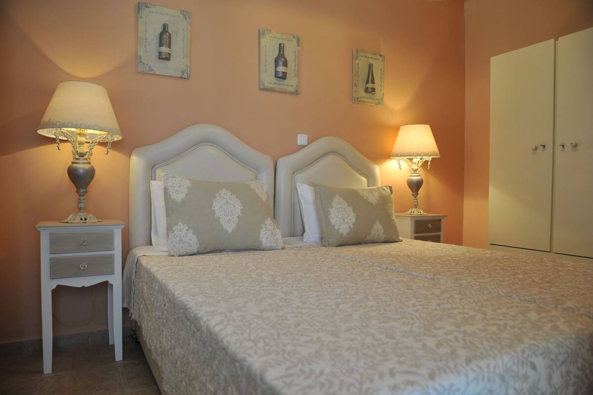 A bedroom with a double bed, two bedside tables with lamps, a wardrobe, and three framed pictures on the wall.