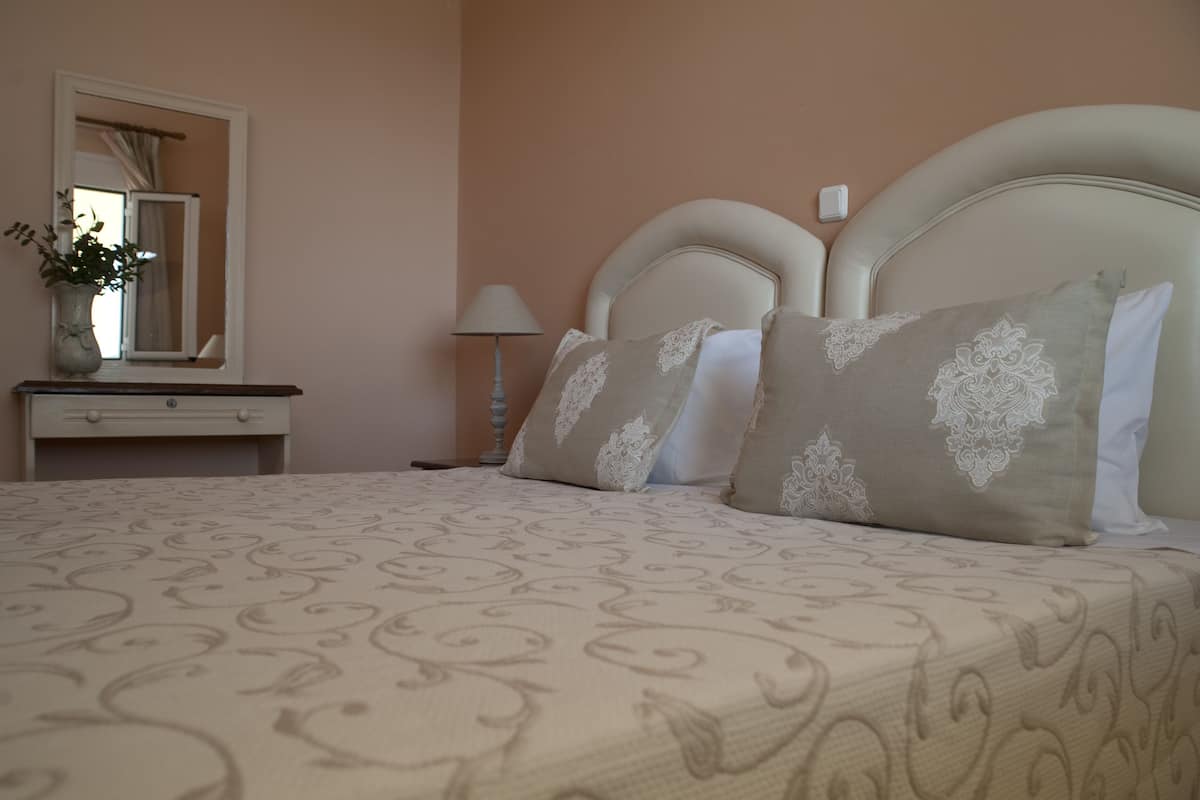 A neatly made bed with a patterned bedspread, a bedside table with a lamp, and a mirror above a dresser.